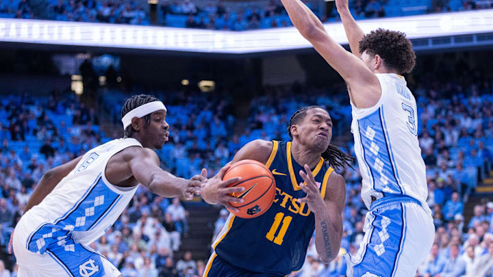 Dec 16, 2025; Chapel Hill, North Carolina, USA; ETSU Buccaneers guard Brian Taylor (11) drives between North Carolina Tar Heels forward Caleb Wilson (8) and guard Derek Dixon (3) during the first half at Dean E. Smith Center. Mandatory Credit: Scott Kinser-Imagn Images
