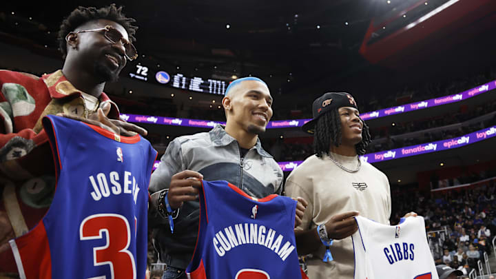 Jan 9, 2025; Detroit, Michigan, USA;  Detroit Lions safety Kerby Joseph (left to right) wide receiver Amon-Ra St. Brown and running back Jahmyr Gibbs hold up jerseys during the second half of the game between the Detroit Pistons and the Golden State Warriors at Little Caesars Arena. Mandatory Credit: Rick Osentoski-Imagn Images
