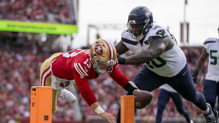 November 17, 2024; Santa Clara, California, USA; San Francisco 49ers quarterback Brock Purdy (13) scores a touchdown against Seattle Seahawks defensive tackle Jarran Reed (90) during the first quarter at Levi's Stadium. Mandatory Credit: Kyle Terada-Imagn Images