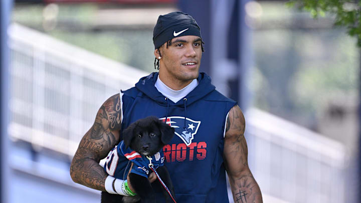 Jul 23, 2025; Foxborough, MA, USA; New England Patriots cornerback Christian Gonzalez (0) delivers a puppy to a local family as part of the Patriots pet adoption event before training camp at Gillette Stadium. Mandatory Credit: Eric Canha-Imagn Images