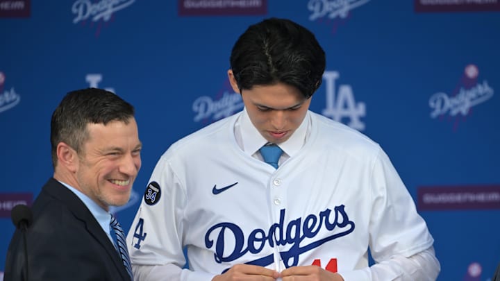 Jan 22, 2025; Los Angeles, CA, USA;  Andrew Friedman, President of baseball operations assists Los Angeles Dodgers pitcher Roki Sasaki (11) with his jersey during a press conference at Dodger Stadium. Mandatory Credit: Jayne Kamin-Oncea-Imagn Images  