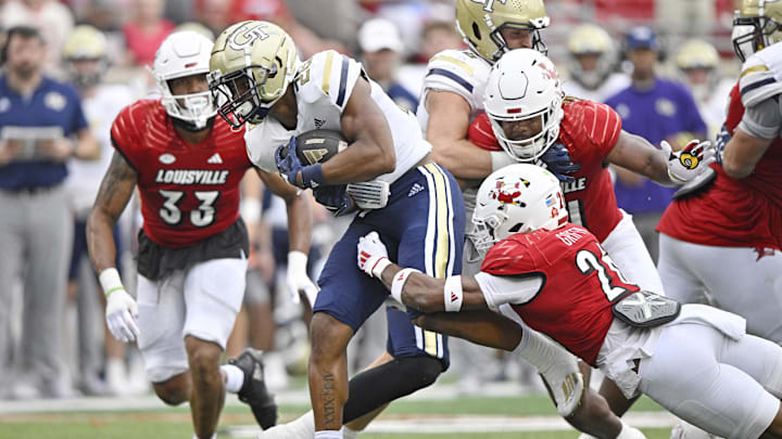 Sep 21, 2024; Louisville, Kentucky, USA;  Georgia Tech Yellow Jackets running back Trelain Maddox (28) tries to break free from the tackle of Louisville Cardinals defensive back M.J. Griffin (26) during the second half at L&N Federal Credit Union Stadium. Mandatory Credit: Jamie Rhodes-Imagn Images