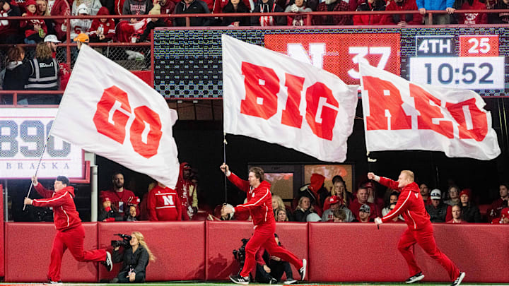 Nov 23, 2024; Lincoln, Nebraska, USA; Nebraska Cornhuskers cheerleaders carry flags across the field after a score against the Wisconsin Badgers during the fourth quarter at Memorial Stadium. Mandatory Credit: Dylan Widger-Imagn Images
