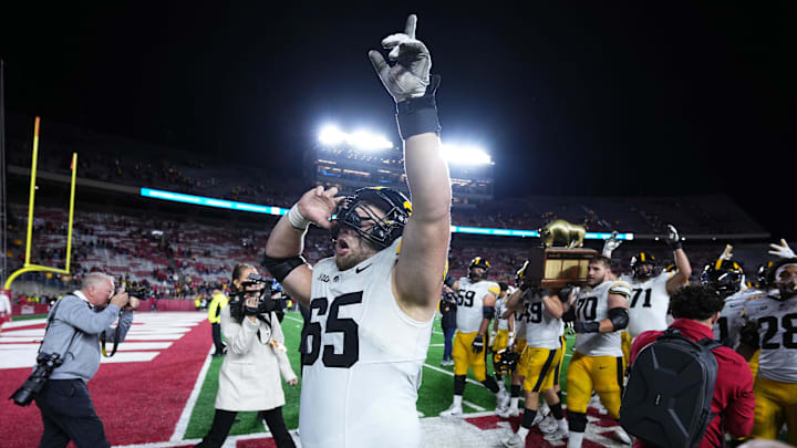 Oct 11, 2025; Madison, Wisconsin, USA; Iowa Hawkeyes offensive lineman Logan Jones (65) celebrates a win after the game against the Wisconsin Badgers while teammates carry The Heartland Trophy in the background at Camp Randall Stadium. Mandatory Credit: Ross Harried-Imagn Images Oct 11, 2025; Madison, Wisconsin, USA; Iowa Hawkeyes offensive lineman Logan Jones (65) celebrates a win after the game against the Wisconsin Badgers while teammates carry The Heartland Trophy in the background at Camp Randall Stadium. Mandatory Credit: Ross Harried-Imagn Images