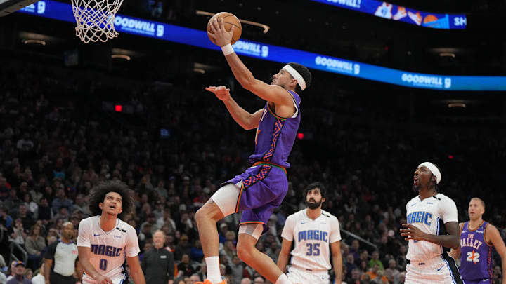 Nov 18, 2024; Phoenix, Arizona, USA; Phoenix Suns guard Devin Booker (1) scores a basket in between Orlando Magic guard Anthony Black (0), center Goga Bitadze (35), and guard Jalen Suggs (4) during the first half of an NBA game at Footprint Center. Mandatory Credit: Rick Scuteri-Imagn Images