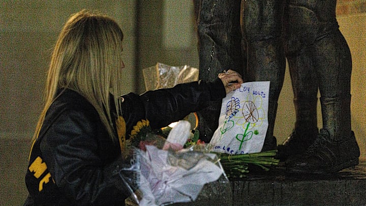 Katie Inhabit Bell places a drawing of flowers done by her 5-year-old daughter Lucy Bell on the statue of Lou Holtz outside of Notre Dame Stadium on Wednesday, March 4, 2026, in South Bend. Holtz, who died earlier in the day, was the head coach of Notre Dame football from 1986-1996, leading the team to a national championship in 1988.