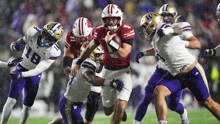 Nov 8, 2025; Madison, Wisconsin, USA;  Wisconsin Badgers quarterback Carter Smith (5) rushes with the football between Washington Huskies linebacker Deven Bryant (17) and defensive lineman Ta'ita'i Uiagalelei (11) during the third quarter at Camp Randall Stadium. Mandatory Credit: Jeff Hanisch-Imagn Images