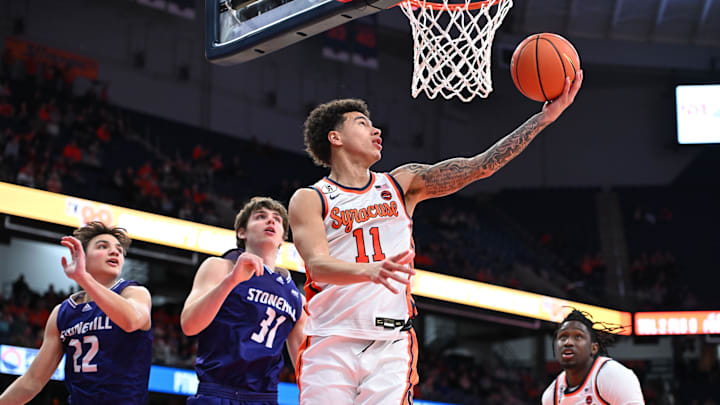 Dec 22, 2025; Syracuse, New York, USA; Syracuse Orange guard Naithan George (11) makes a reverse lay up over the defense of Stonehill Skyhawks forward Pearse McGuinn (31) and guard Charlie Diamantis (22) in the second half at the JMA Wireless Dome. Mandatory Credit: Mark Konezny-Imagn Images Dec 22, 2025; Syracuse, New York, USA; Syracuse Orange guard Naithan George (11) makes a reverse lay up over the defense of Stonehill Skyhawks forward Pearse McGuinn (31) and guard Charlie Diamantis (22) in the second half at the JMA Wireless Dome. Mandatory Credit: Mark Konezny-Imagn Images