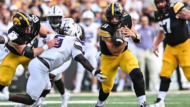 Aug 30, 2025; Iowa City, Iowa, USA; Iowa Hawkeyes quarterback Mark Gronowski (11) clutches the ball as offensive lineman Logan Jones (65) blocks and Albany Great Danes linebacker Ron Holmes (5) looks to make the tackle during the first quarter at Kinnick Stadium. Mandatory Credit: Jeffrey Becker-Imagn Images