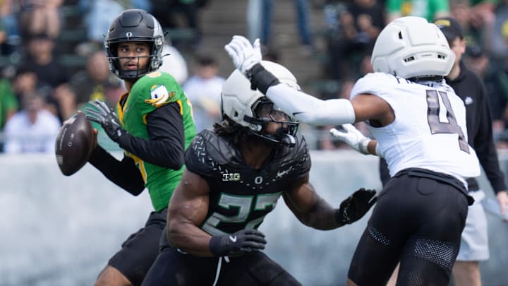 Combat Duck Dante Moore, left, drops back to pass behind a block by Jay Harris against Fighting Duck 
Brandon Finny during the fourth quarter of the Oregon Spring Game.