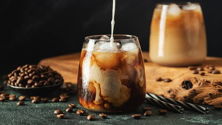 Milk poured into iced coffee drink in glass 