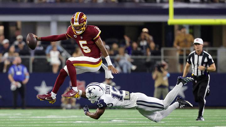 Washington Commanders quarterback Jayden Daniels (5) leaps to avoid a tackle by Dallas Cowboys safety Caleb Downs (13) while running with the ball during the second half at AT&T Stadium. 