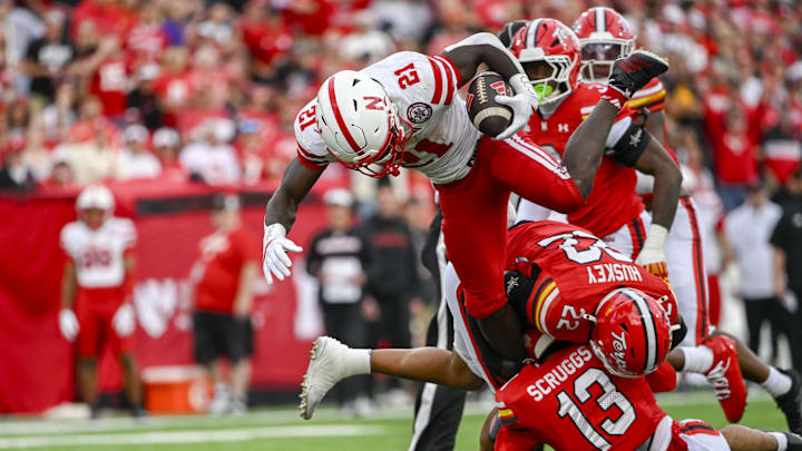 Oct 11, 2025; College Park, Maryland, USA;  Nebraska Cornhuskers running back Emmett Johnson (21) leaps as Maryland Terrapins defensive back Lavain Scruggs (13) and defensive back Jalen Huskey (22) attempt to tackle during the first half at SECU Stadium. Mandatory Credit: Tommy Gilligan-Imagn Images