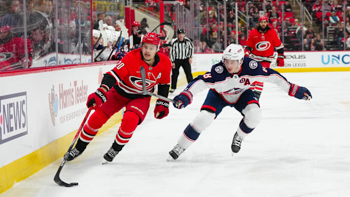 Jan 23, 2025; Raleigh, North Carolina, USA;  Carolina Hurricanes center Sebastian Aho (20) and Columbus Blue Jackets defenseman Zach Werenski (8) chase after the puck during the first period at Lenovo Center. Mandatory Credit: James Guillory-Imagn Images