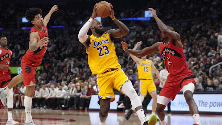 Nov 1, 2024; Toronto, Ontario, CAN; Los Angeles Lakers forward LeBron James (23) tries to go in between Toronto Raptors forward Jonathan Mogbo (2) and guard D.J. Carton (3)  during the first half at Scotiabank Arena. Mandatory Credit: John E. Sokolowski-Imagn Images
