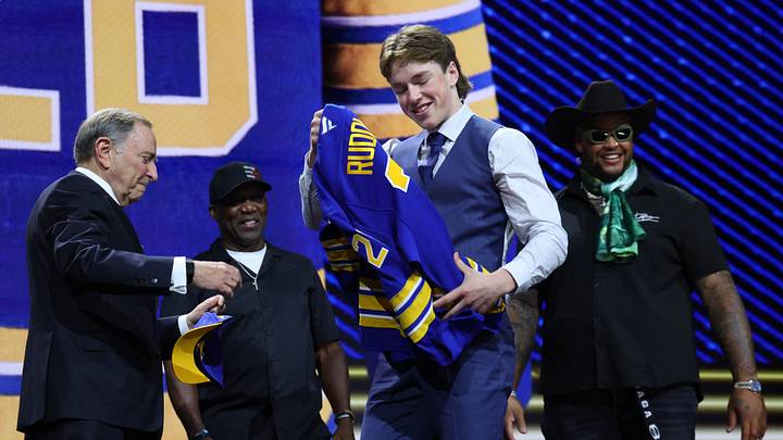 Daxon Rudolph takes a sweater from NHL commissioner Gary Bettman in front of former Buffalo Bills player Thurman Thomas and current Bills player Dion Dawkins watch after being selected with the fourth pick in the first round of the 2026 NHL Draft by the Buffalo Sabres at KeyBank Center. Mandatory Credit: Timothy T. Ludwig-Imagn Images Daxon Rudolph takes a sweater from NHL commissioner Gary Bettman in front of former Buffalo Bills player Thurman Thomas and current Bills player Dion Dawkins watch after being selected with the fourth pick in the first round of the 2026 NHL Draft by the Buffalo Sabres at KeyBank Center. Mandatory Credit: Timothy T. Ludwig-Imagn Images