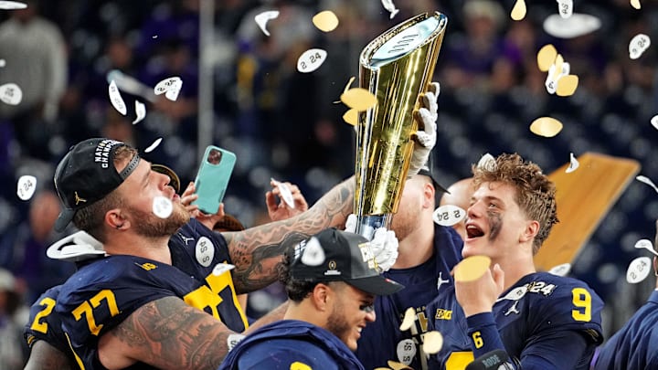 Michigan Wolverines offensive lineman Trevor Keegan (77) and quarterback J.J. McCarthy (9) celebrate with CFP National Championship trophy after defeating the Washington Huskies in the 2024 College Football Playoff.