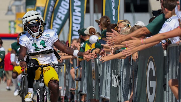 Green Bay Packers wide receiver Jayden Reed (11) slaps hands with fans as he rides a bicycle to practice at training camp last year.