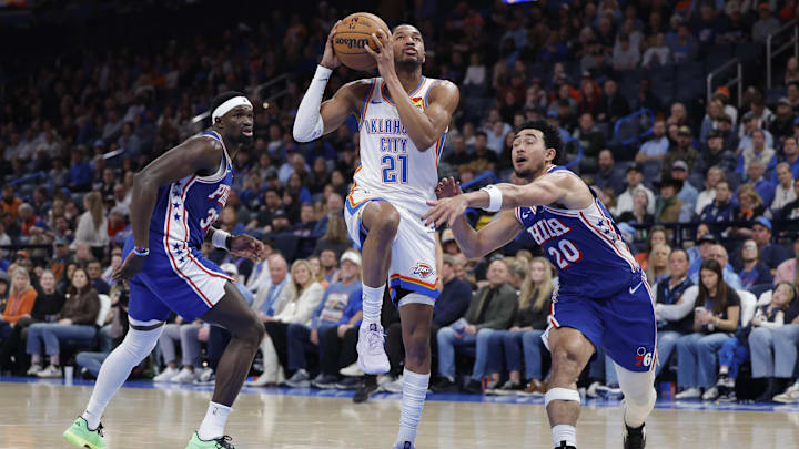 Dec 28, 2025; Oklahoma City, Oklahoma, USA; Oklahoma City Thunder guard Aaron Wiggins (21) drives between Philadelphia 76ers center Adem Bona (30) and guard Jared McCain (20) during the second half at Paycom Center. Mandatory Credit: Alonzo Adams-Imagn Images