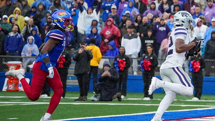 Oct 25, 2025; Lawrence, Kansas, USA; Kansas State Wildcats wide receiver Jaron Tibbs (12) scores a touchdown as Kansas Jayhawks defensive back Austin Alexander (0) chases during the first half of the game at David Booth Kansas Memorial Stadium. Mandatory Credit: Denny Medley-Imagn Images