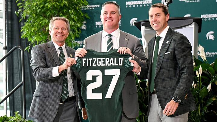 Michigan State football's new coach Pat Fitzgerald, center, holds up a jersey with MSU president Kevin Guskiewicz, left, and athletic director J Batt, right Michigan State football's new coach Pat Fitzgerald, center, holds up a jersey with MSU president Kevin Guskiewicz, left, and athletic director J Batt, right