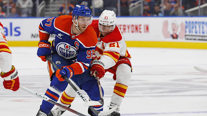 Sep 23, 2024; Edmonton, Alberta, CAN; Calgary Flames forward Kevin Rooney (21) tries to knock the puck away from Edmonton Oilers forward Connor McDavid (97) during the third period  at Rogers Place. Mandatory Credit: Perry Nelson-Imagn Images