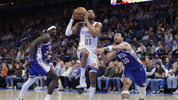 Dec 28, 2025; Oklahoma City, Oklahoma, USA; Oklahoma City Thunder guard Aaron Wiggins (21) drives between Philadelphia 76ers center Adem Bona (30) and guard Jared McCain (20) during the second half at Paycom Center. Mandatory Credit: Alonzo Adams-Imagn Images
