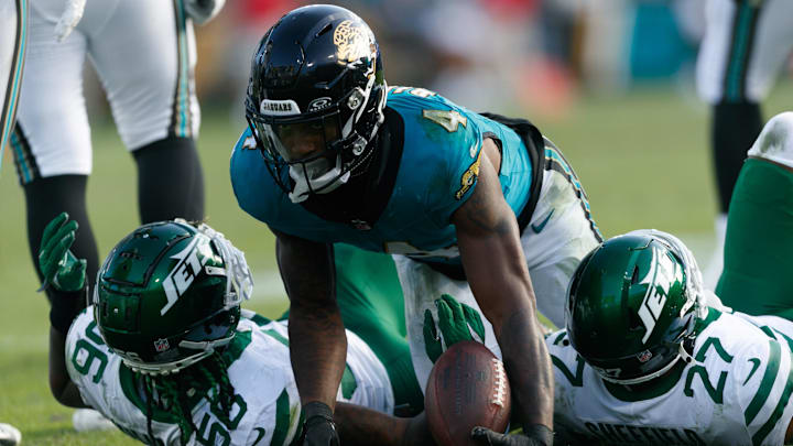 Dec 15, 2024; Jacksonville, Florida, USA; Jacksonville Jaguars running back Tank Bigsby (4) stands after being tackled by New York Jets linebacker Quincy Williams (56) and cornerback Kendall Sheffield (27) during the fourth quarter at EverBank Stadium. Mandatory Credit: Morgan Tencza-Imagn Images