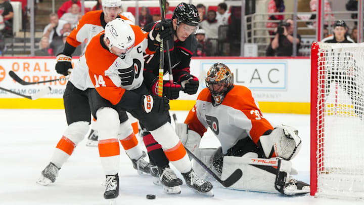 Oct 11, 2025; Raleigh, North Carolina, USA;  Carolina Hurricanes defenseman Alexander Nikishin (21) and Philadelphia Flyers center Sean Couturier (14) battle over the loose puck in from of Philadelphia Flyers goaltender Samuel Ersson (33) during the third period at Lenovo Center. Mandatory Credit: James Guillory-Imagn Images