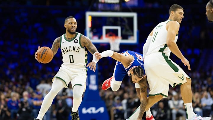 Oct 23, 2024; Philadelphia, Pennsylvania, USA; Milwaukee Bucks guard Damian Lillard (0) dribbles past Philadelphia 76ers forward Caleb Martin (16) and Bucks Brook Lopez (11) during the second quarter at Wells Fargo Center. Mandatory Credit: Bill Streicher-Imagn Images