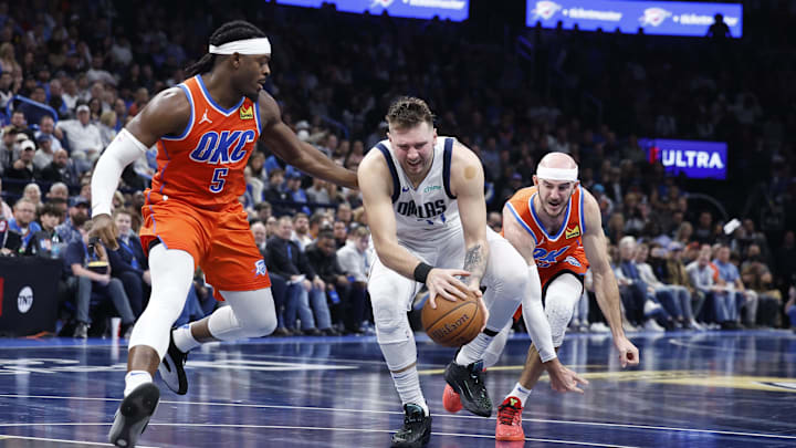Dec 10, 2024; Oklahoma City, Oklahoma, USA; Dallas Mavericks guard Luka Doncic (77) drives between Oklahoma City Thunder guard Luguentz Dort (5) and guard Alex Caruso (9) during the second half at Paycom Center. Mandatory Credit: Alonzo Adams-Imagn Images Dec 10, 2024; Oklahoma City, Oklahoma, USA; Dallas Mavericks guard Luka Doncic (77) drives between Oklahoma City Thunder guard Luguentz Dort (5) and guard Alex Caruso (9) during the second half at Paycom Center. Mandatory Credit: Alonzo Adams-Imagn Images