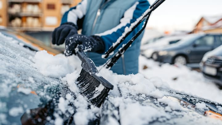 Hombre mayor quitando la nieve de su coche en el parking