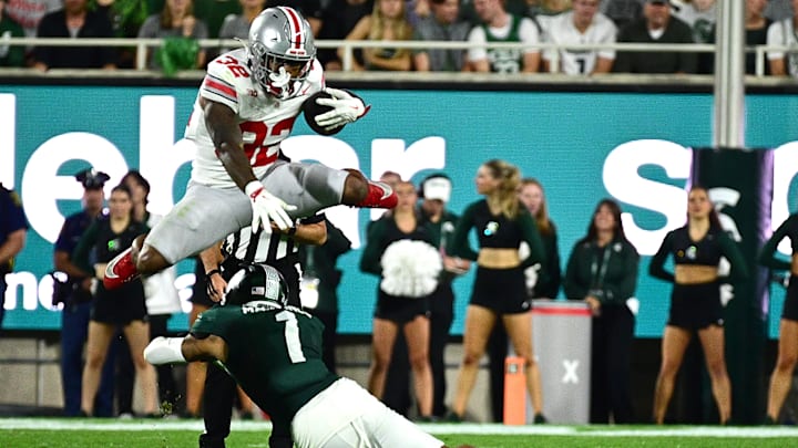 Sep 28, 2024; East Lansing, Michigan, USA;  Ohio State Buckeyes running back TreVeyon Henderson (32) leaps over Michigan State Spartans defensive back Nikai Martinez (1) in the first quarter at Spartan Stadium. 