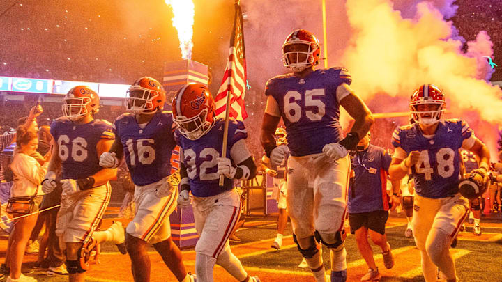Florida Gators offensive lineman Brandon Crenshaw-Dickson (65) leaps in the air as Florida Gators defensive back Cahron Rackley (32) carries the American flag while running out of the tunnel with the team as fireworks and fire shoot out of towers before the start of the game at Ben Hill Griffin Stadium in Gainesville, FL on Saturday, October 5, 2024. [Doug Engle/Gainesville Sun]
