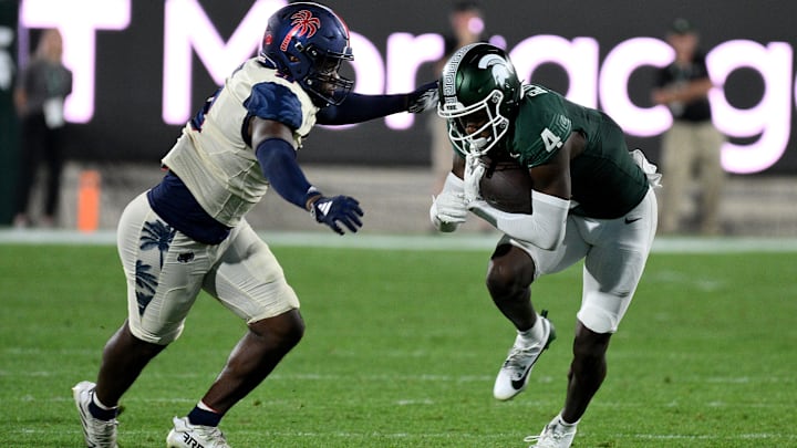 Aug 30, 2024; East Lansing, Michigan, USA;  Michigan State Spartans wide receiver Jaron Glover (4) runs from Florida Atlantic Owls cornerback Logic Hudgens (8) in the third quarter at Spartan Stadium. Mandatory Credit: Dale Young-Imagn Images