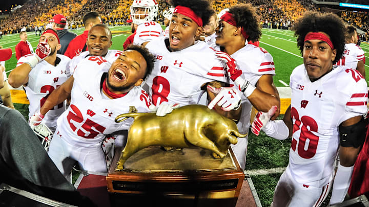 Sep 22, 2018; Iowa City, IA, USA; Wisconsin Badgers safety Eric Burrell (25) and cornerback Deron Harrell (8) and cornerback Travian Blaylock (26) and teammates surround the Heartland Trophy after defeating the Iowa Hawkeyes at Kinnick Stadium. Mandatory Credit: Jeffrey Becker-Imagn Images Sep 22, 2018; Iowa City, IA, USA; Wisconsin Badgers safety Eric Burrell (25) and cornerback Deron Harrell (8) and cornerback Travian Blaylock (26) and teammates surround the Heartland Trophy after defeating the Iowa Hawkeyes at Kinnick Stadium. Mandatory Credit: Jeffrey Becker-Imagn Images