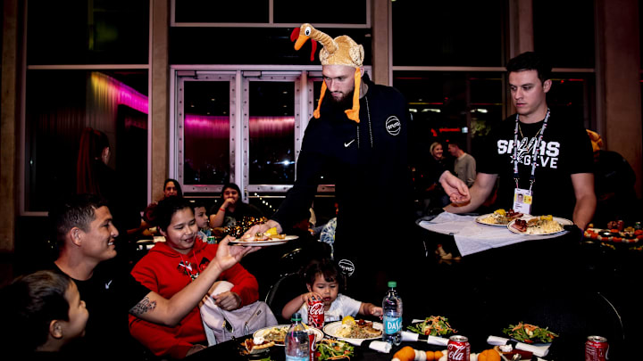 Nov. 20, 2024; San Antonio, Texas, USA; San Antonio Spurs power forward Sandro Mamukelashvili (54), wearing a turkey, hat, hands out plates of food to families at the Spurs' Season of Giving Dinner at Frost Bank Center. 