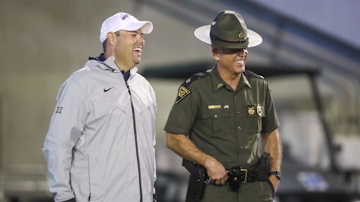 Sep 9, 2023; Morgantown, West Virginia, USA; West Virginia University Athletic Director Wren Baker talks to a West Virginia State Trooper during the third quarter against the Duquesne Dukes at Mountaineer Field at Milan Puskar Stadium. Mandatory Credit: Ben Queen-Imagn Images