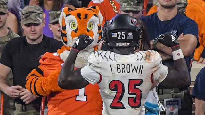 Nov 2, 2024; Clemson, South Carolina, USA; Louisville Cardinals running back Isaac Brown (25) flexes his muscles in front of the Clemson Tigers Tiger mascot after scoring in the fourth quarter at Memorial Stadium. Mandatory Credit: Ken Ruinard-Imagn Images