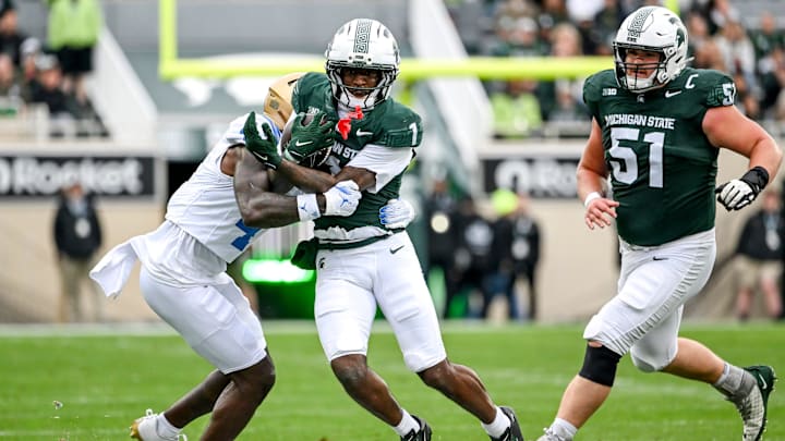 Michigan State's Omari Kelly, center, runs for a gain as UCLA's Key Lawrence closes in during the first quarter on Saturday, Oct. 11, 2025, at Spartan Stadium in East Lansing.