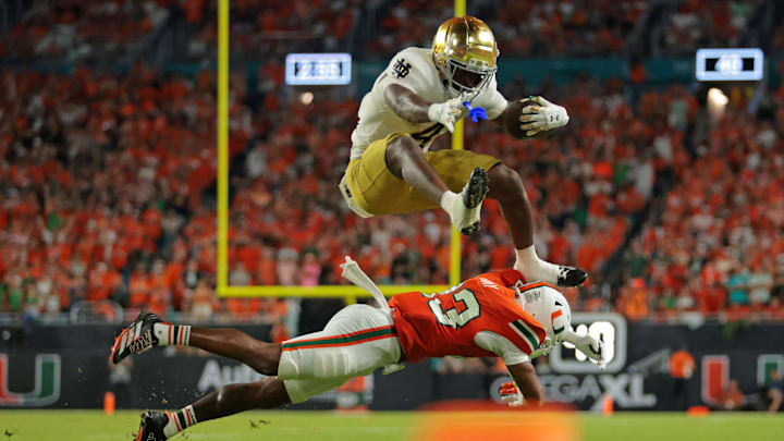 Aug 31, 2025; Miami Gardens, Florida, USA; Notre Dame Fighting Irish running back Jeremiyah Love (4) hurdles over Miami Hurricanes defensive back Dylan Day (23) during the third quarter at Hard Rock Stadium. Mandatory Credit: Sam Navarro-Imagn Images