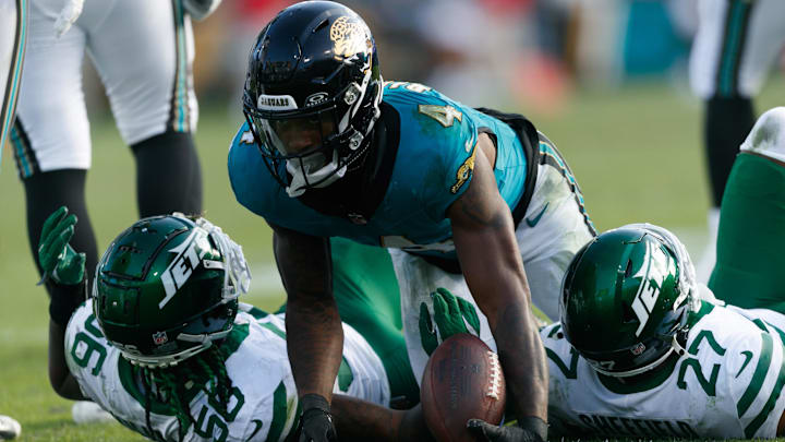 Dec 15, 2024; Jacksonville, Florida, USA; Jacksonville Jaguars running back Tank Bigsby (4) stands after being tackled by New York Jets linebacker Quincy Williams (56) and cornerback Kendall Sheffield (27) during the fourth quarter at EverBank Stadium. Mandatory Credit: Morgan Tencza-Imagn Images Dec 15, 2024; Jacksonville, Florida, USA; Jacksonville Jaguars running back Tank Bigsby (4) stands after being tackled by New York Jets linebacker Quincy Williams (56) and cornerback Kendall Sheffield (27) during the fourth quarter at EverBank Stadium. Mandatory Credit: Morgan Tencza-Imagn Images