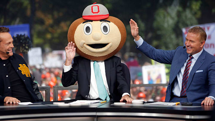 ESPN's Lee Corso, center, waves his hand after putting the Ohio State Buckeyes mascot head on to end \"College GameDay\" Saturday at Notre Dame. To the left is actor Vince Vaughn, and to the right is ESPN's Kirk Herbstreit.