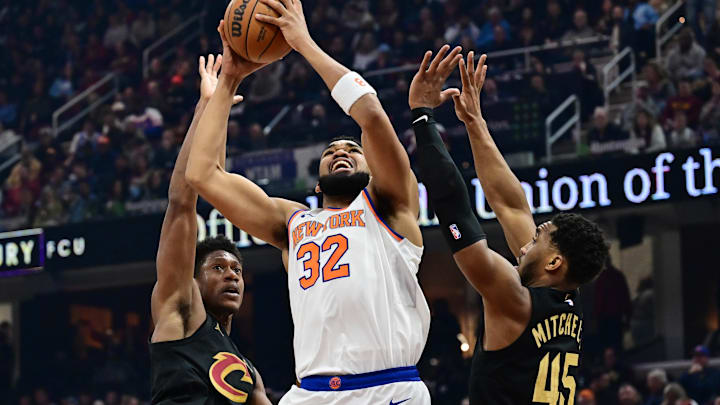Feb 21, 2025; Cleveland, Ohio, USA;  New York Knicks center Karl-Anthony Towns (32) drives to the basket between Cleveland Cavaliers forward De'Andre Hunter (12) and guard Donovan Mitchell (45) during the first half at Rocket Arena. Mandatory Credit: Ken Blaze-Imagn Images