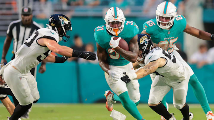 Miami Dolphins running back Ollie Gordon II (31) runs with the football past Jacksonville Jaguars linebacker Dennis Gardeck (57) and linebacker Branson Combs (50) during the second quarter at Hard Rock Stadium. 
