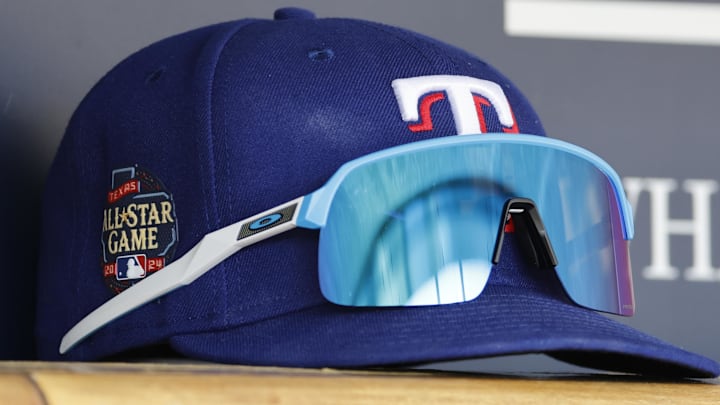 Texas Rangers cap sits in dugout with sunglasses across the front. Texas Rangers cap sits in dugout with sunglasses across the front.