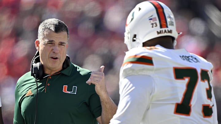 Oct 19, 2024; Louisville, Kentucky, USA; Miami Hurricanes head coach Mario Cristobal talks with offensive lineman Anez Cooper (73) during the first half against the Louisville Cardinals at L&N Federal Credit Union Stadium. Mandatory Credit: Jamie Rhodes-Imagn Images