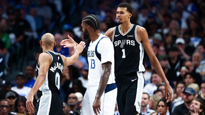 Oct 22, 2025; Dallas, Texas, USA; San Antonio Spurs forward Victor Wembanyama (1) celebrates with guard Jordan McLaughlin (0) in front of Dallas Mavericks forward Naji Marshall (13) during the first half  at American Airlines Center.