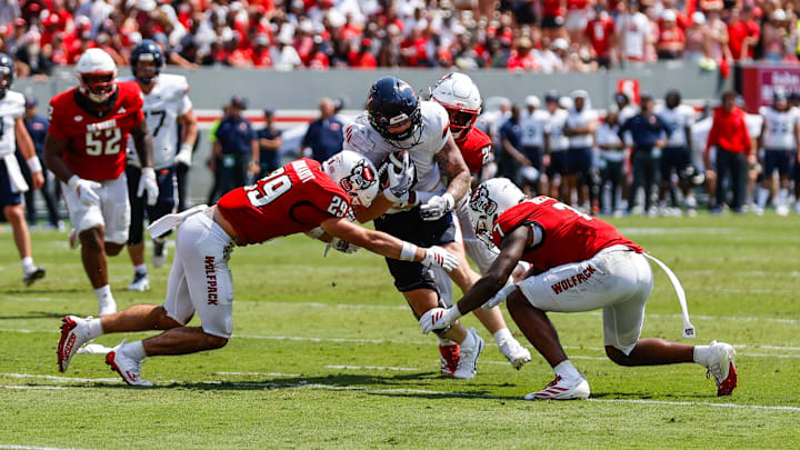 Sep 6, 2025; Raleigh, North Carolina, USA; Virginia Cavaliers tight end Sage Ennis (0) is tackled by North Carolina State Wolfpack safety Brody Barnhardt (29), cornerback Brian Nelson II (7) and cornerback Jackson Vick (22) during the first half of the game at Carter-Finley Stadium. Mandatory Credit: Jaylynn Nash-Imagn Images Sep 6, 2025; Raleigh, North Carolina, USA; Virginia Cavaliers tight end Sage Ennis (0) is tackled by North Carolina State Wolfpack safety Brody Barnhardt (29), cornerback Brian Nelson II (7) and cornerback Jackson Vick (22) during the first half of the game at Carter-Finley Stadium. Mandatory Credit: Jaylynn Nash-Imagn Images