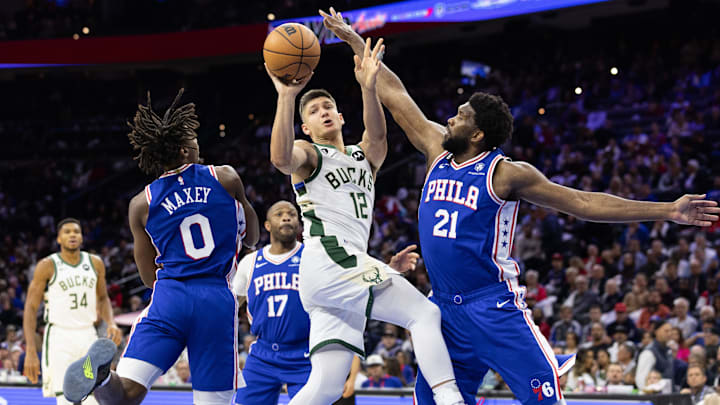 Oct 20, 2022; Philadelphia, Pennsylvania, USA; Milwaukee Bucks guard Grayson Allen (12) passes the ball between Philadelphia 76ers center Joel Embiid (21) and guard Tyrese Maxey (0) during the third quarter at Wells Fargo Center. Mandatory Credit: Bill Streicher-Imagn Images